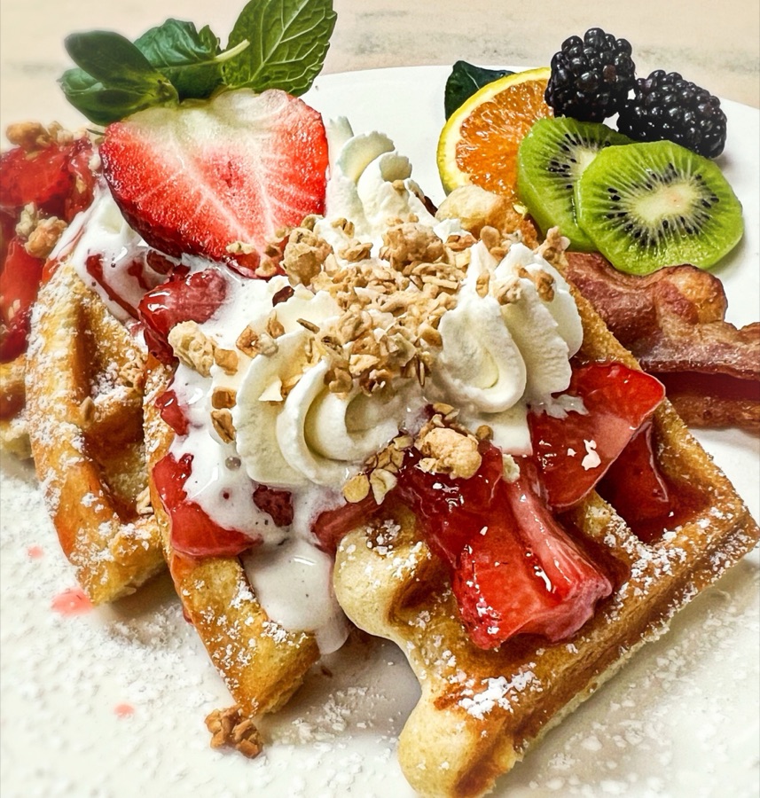 Waffles with strawberries, whipped cream and granola, bacon and fresh fruit