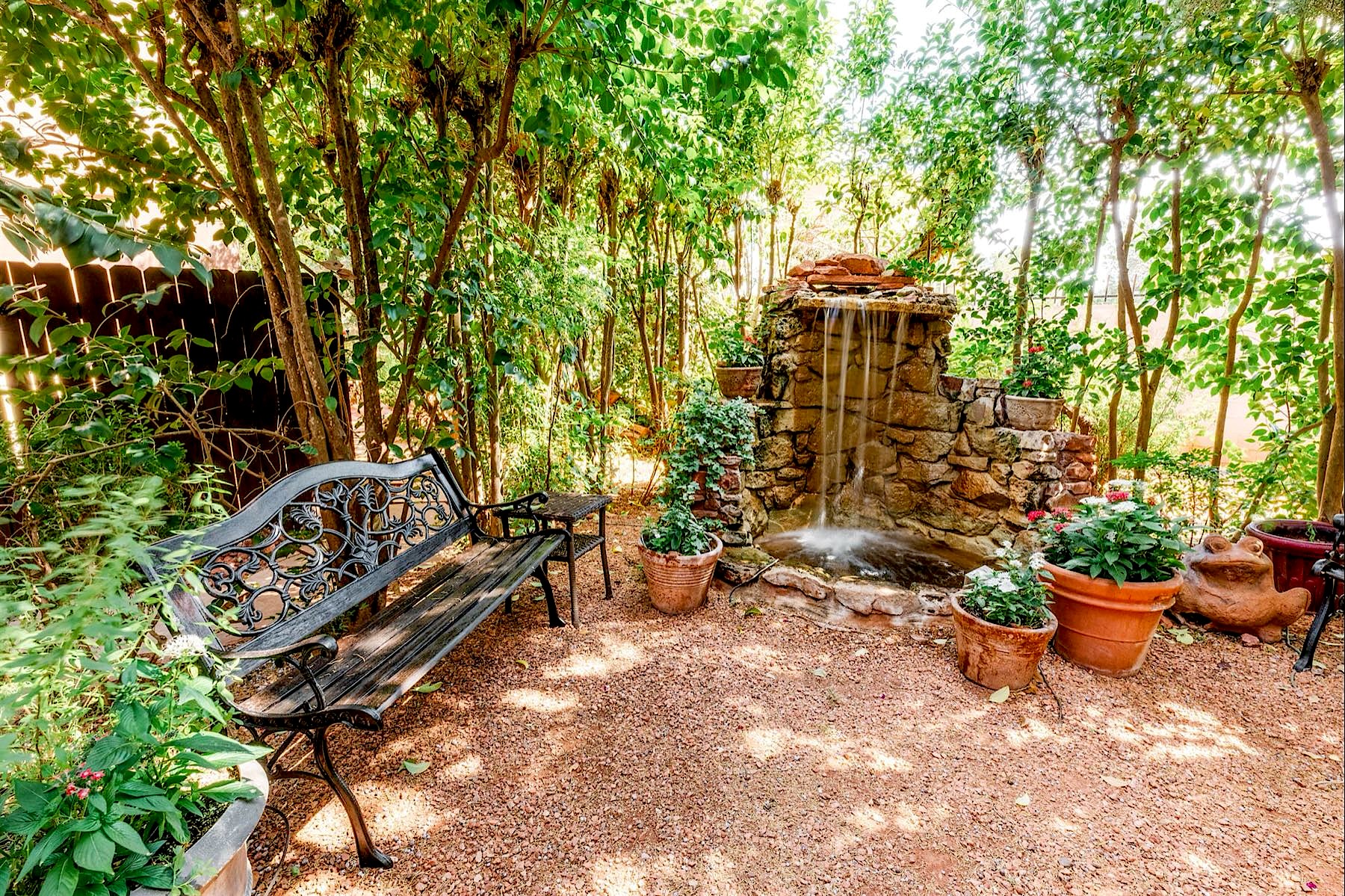 Shaded garden courtyard with a stone waterfall fountain and an iron bench
