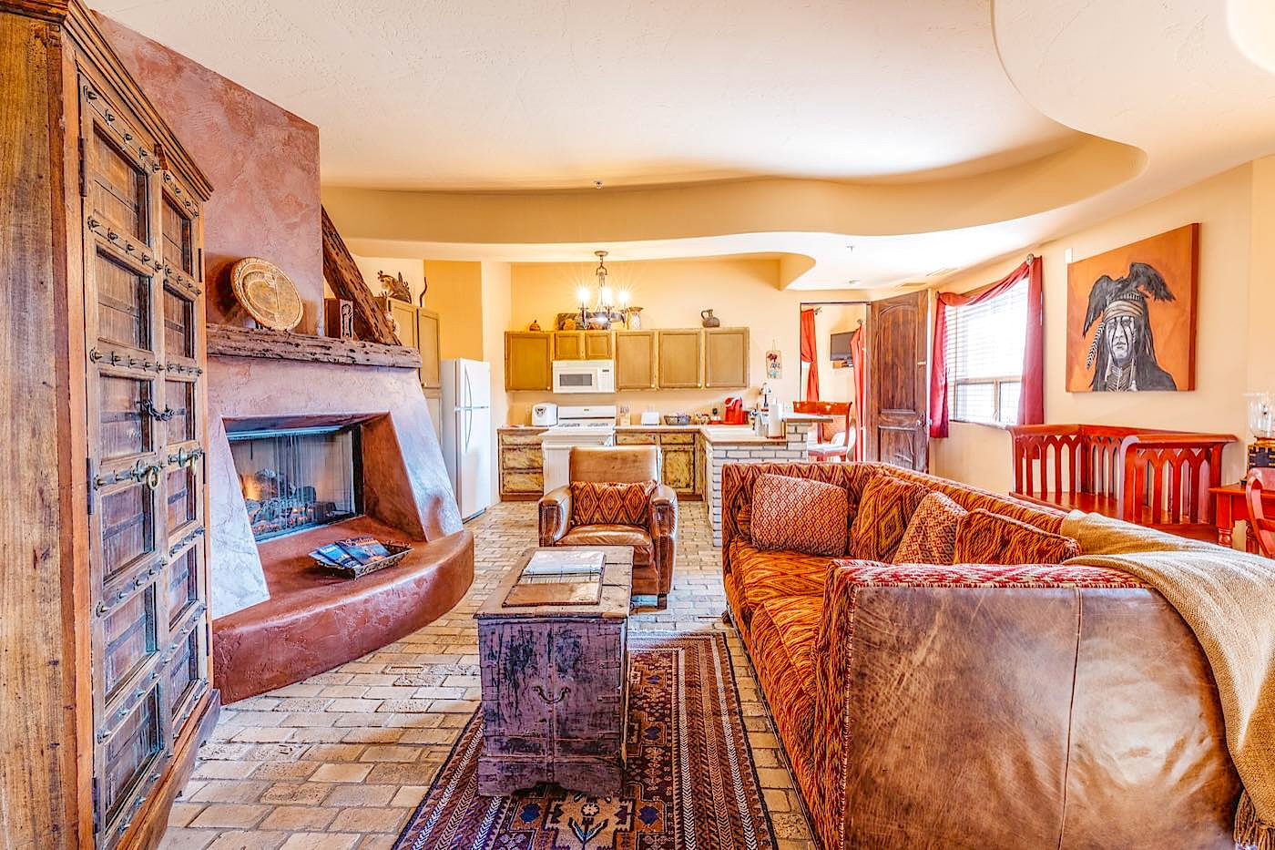 Hacienda villa living room with a kiva fireplace, leather sofa and the kitchen beyond at Adobe Grand Villas in Sedona